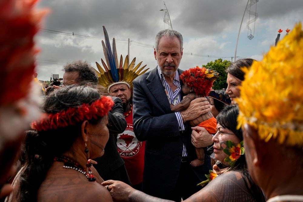 O embaixador André Corrêa do Lago, presidente da COP30, segura o filho da ativista Maria Leusa Munduruku durante as negociações para liberar a entrada da Blue Zone. Ao lado dele está Ana Toni (de perfil), CEO da COP30, e à frente dele aparece a ativista Alessandra Munduruku (Foto: Fernando Martinho/Repórter Brasil)